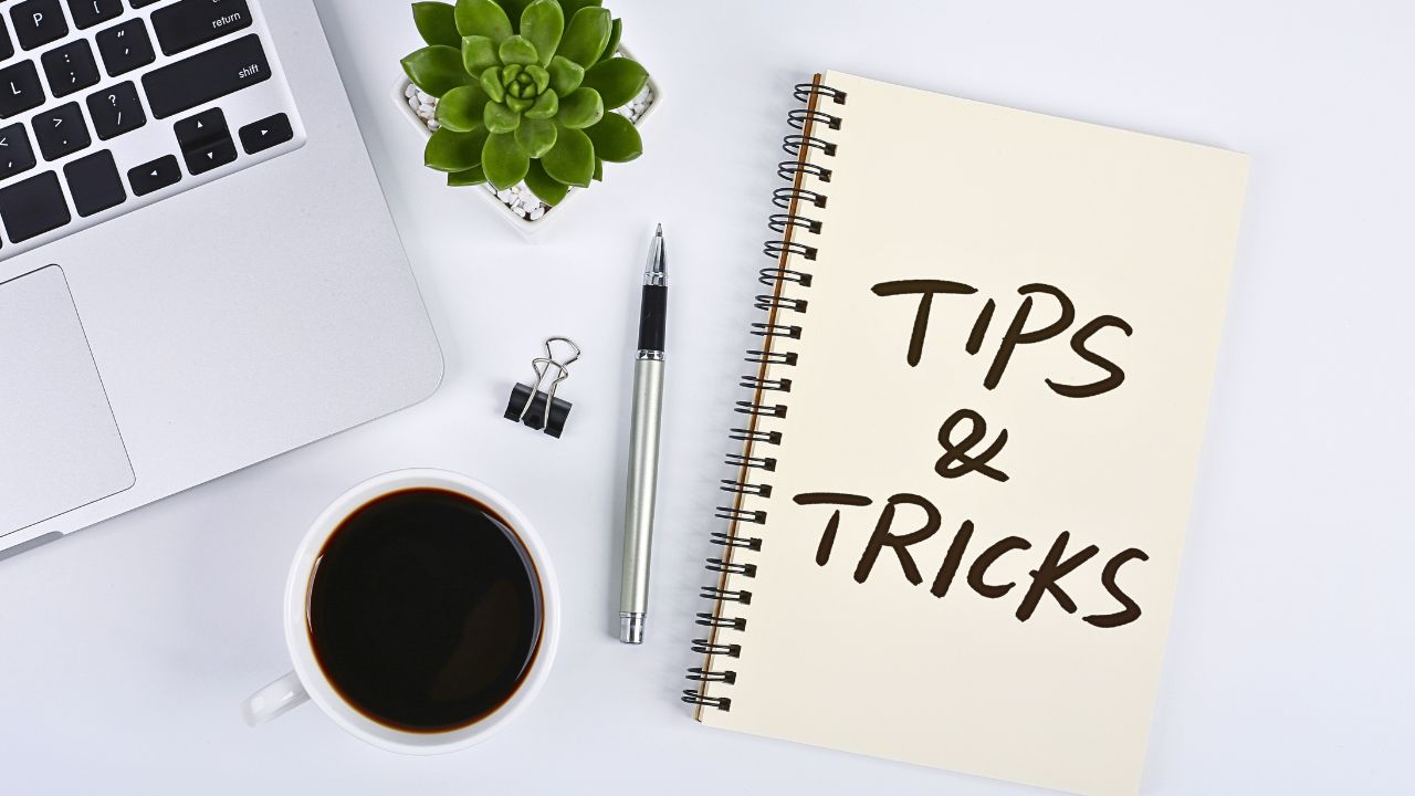 White desk with laptop, coffee cup, plant, and a book titled "Tips and Tricks" symbolizing practical guides and media earning strategies.