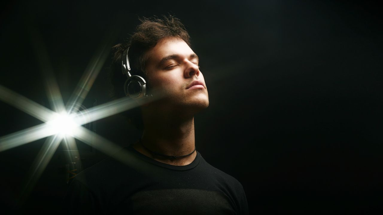 Person wearing headphones standing in front of a black wall with a bright light nearby, representing immersive media experiences and earning opportunities.